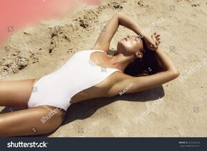 stock-photo-sexy-woman-in-white-swimsuit-is-lying-on-the-sand-beside-a-lake-with-a-pink-water-661553776.jpg