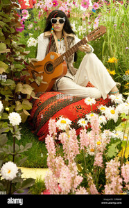 1960-flower-power-figura-vistiendo-sombras-sosteniendo-la-guitarra-sentados-sobre-el-cojin-por-flores-de-colores-brillantes-rhs-flower-show-tatton-park-cheshire-reino-unido-cp9xhp.jpg